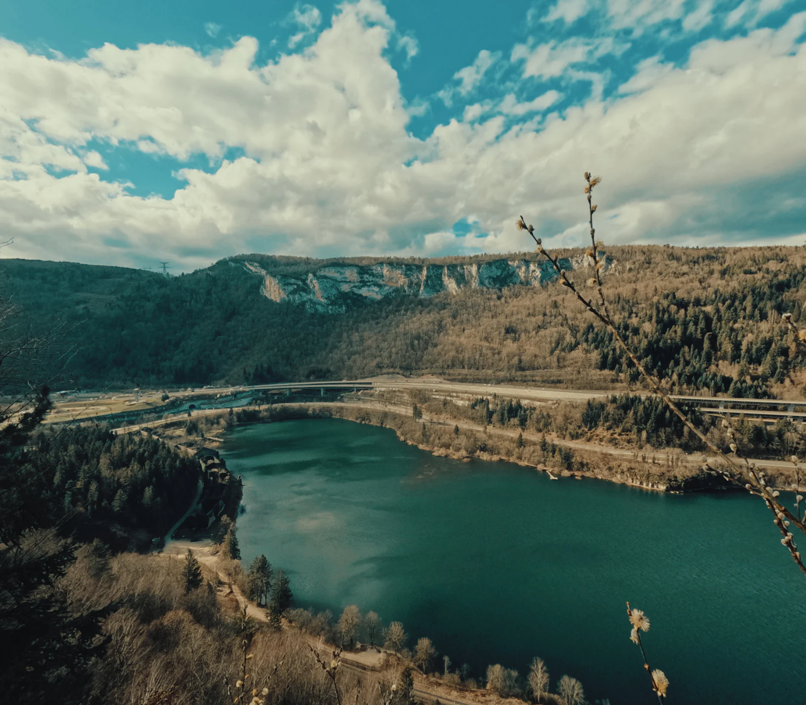 Lac du Jura entre forêts et falaises, sous un ciel nuageux